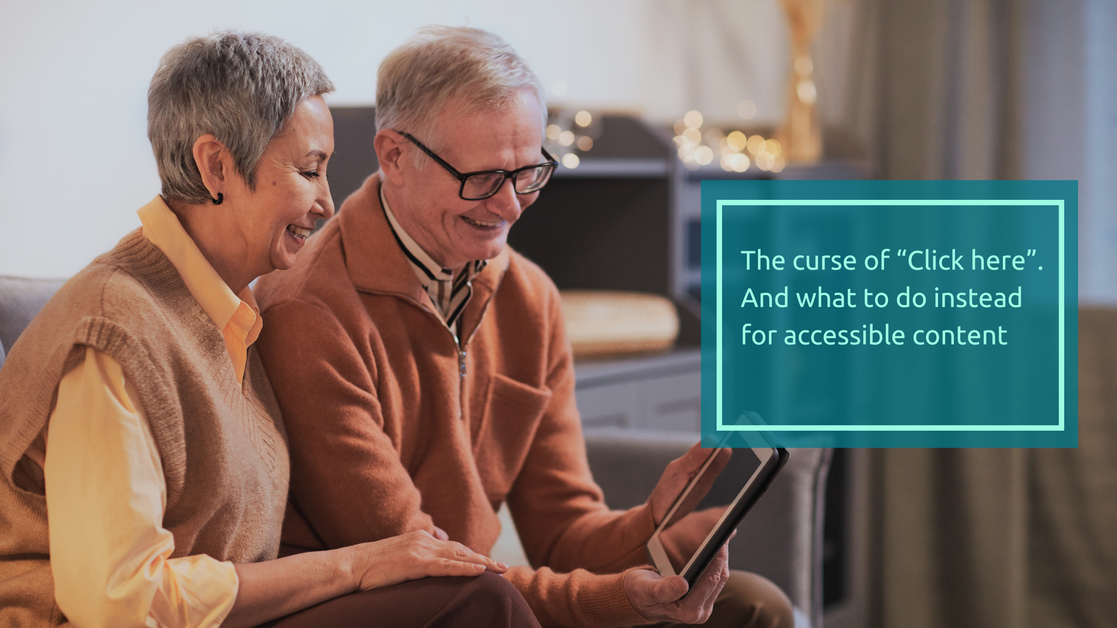 An older couple sitting in their lounge room looking at a mobile phone. The couple are dressed in neutral tones and smiling at the accessible content on the screen